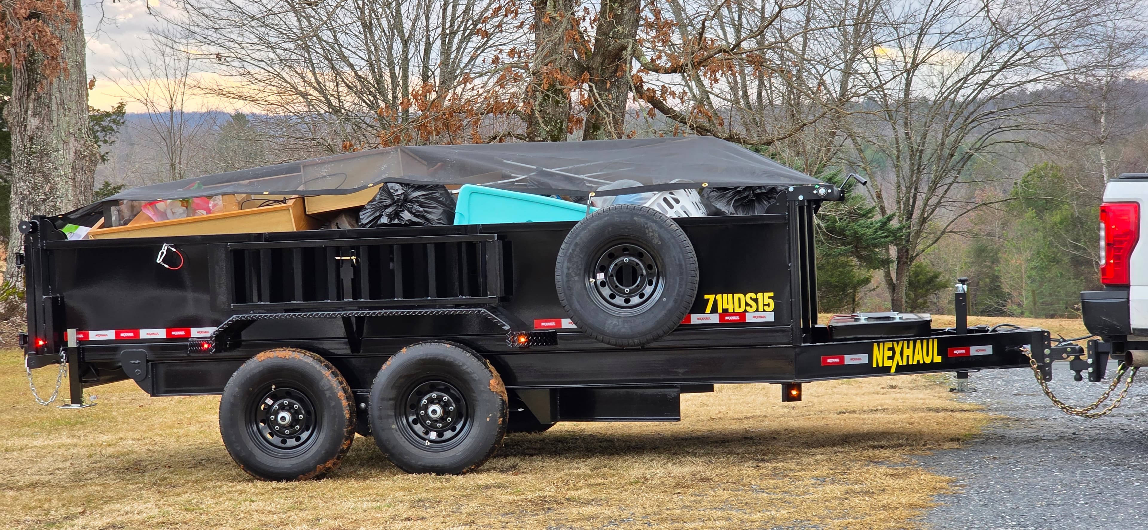 Dump trailer loaded with debris under protective tarp in mountain landscape