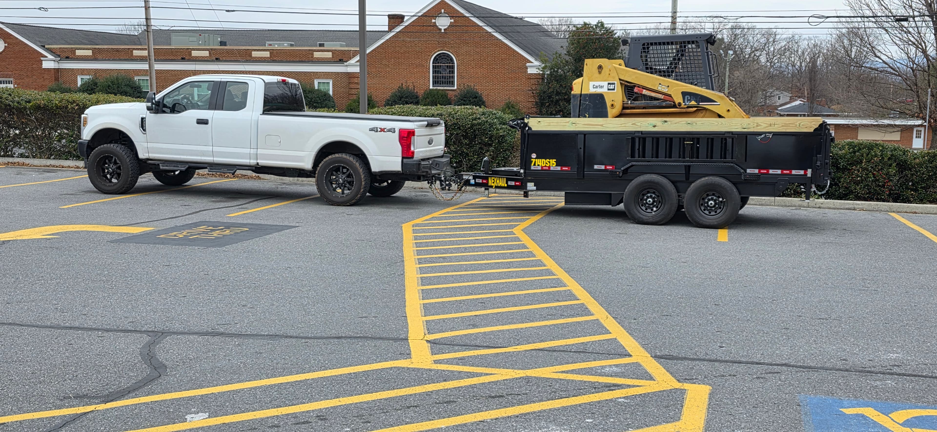 White pickup truck towing dump trailer with Caterpillar skid steer loader mounted on top
