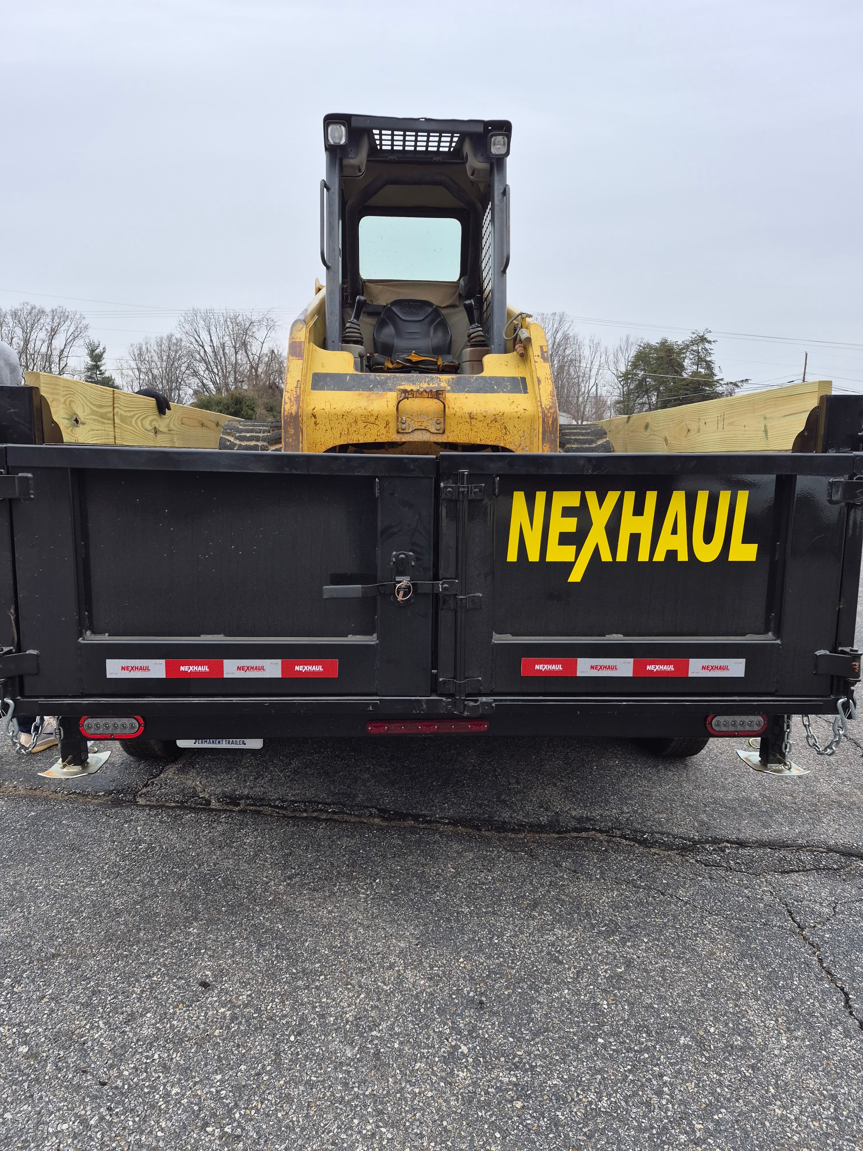 Front view of black dump trailer with yellow Caterpillar skid stew loader mounted securely