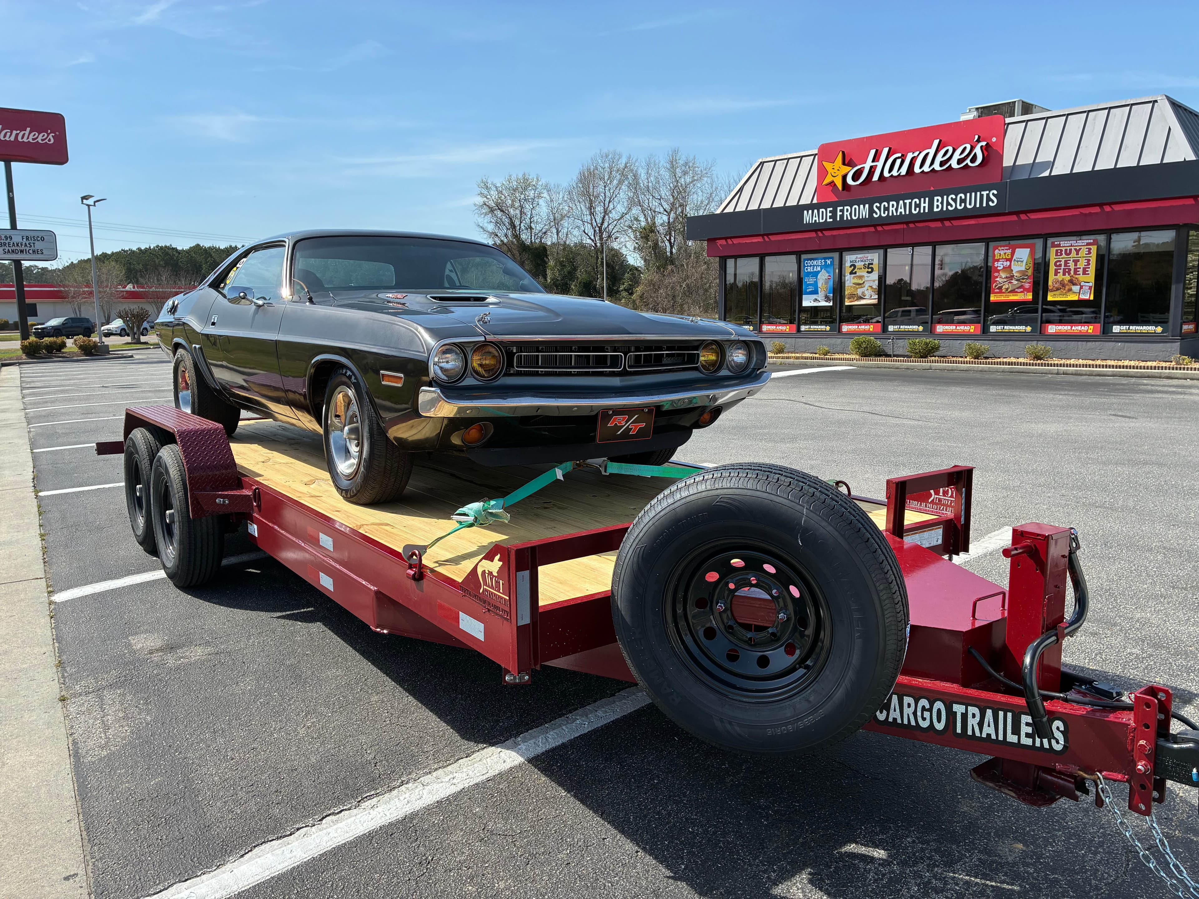 Classic 1970s Dodge Challenger front three-quarter view on red dual-axle cargo trailer with green tie-down straps