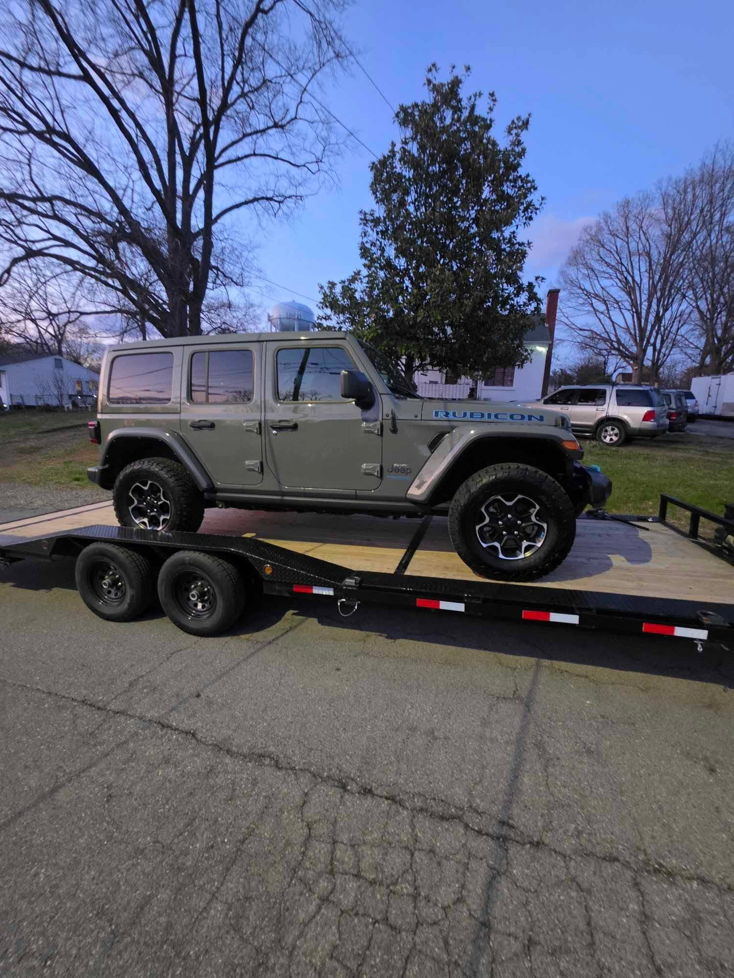Olive green Jeep Wrangler Rubicon 4-door on a black dual-axle car trailer in a parking lot