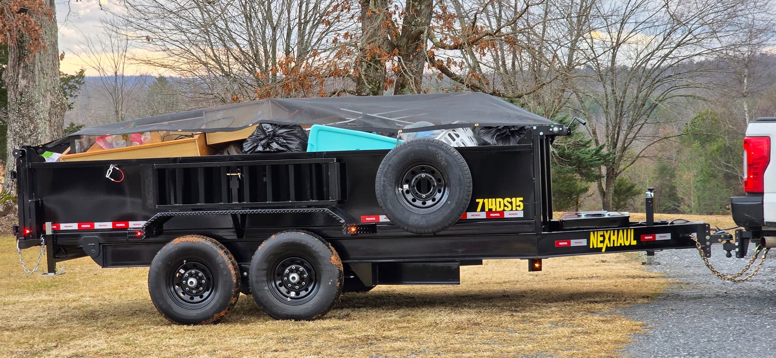 Dump trailer loaded with debris under protective tarp in mountain landscape