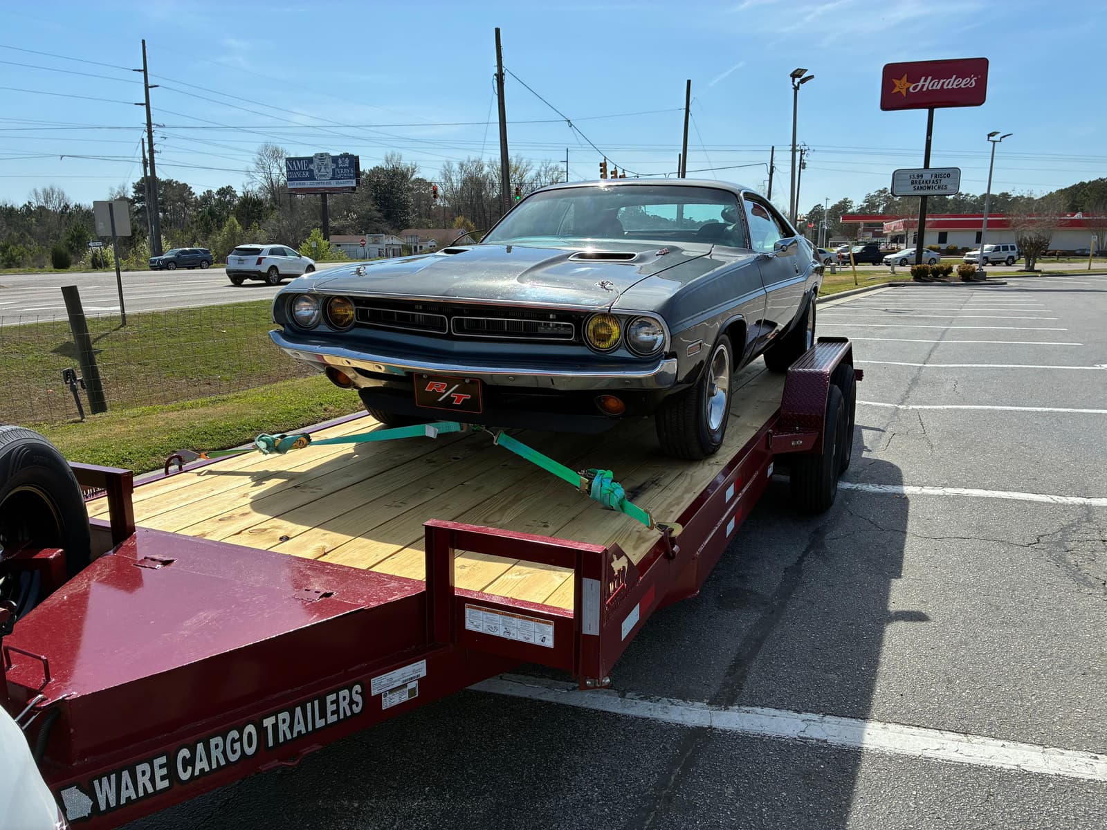 1971 Dodge Challenger R/T loaded on the red J&T car trailer at a Hardee's parking lot, front three-quarter view showing the wood deck and ramps
