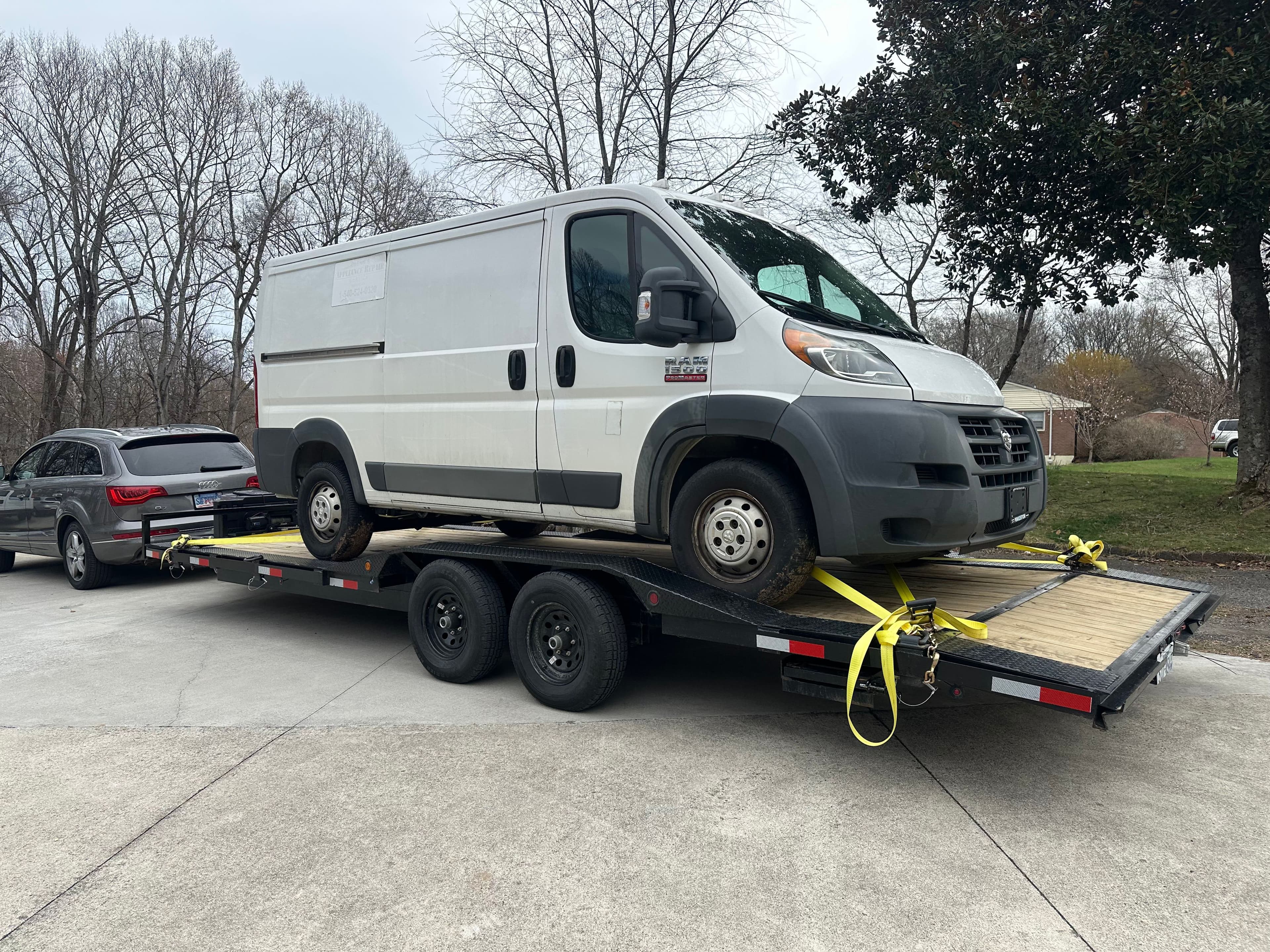 White commercial work van transported on black dual-axle car trailer with yellow tie-down straps