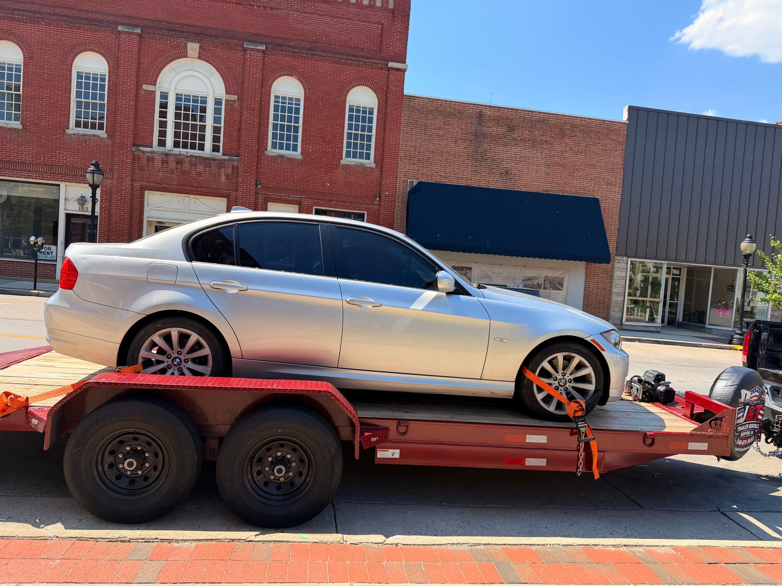 Silver BMW 3 Series side profile on the red J&T car trailer in front of brick buildings in downtown Bedford VA