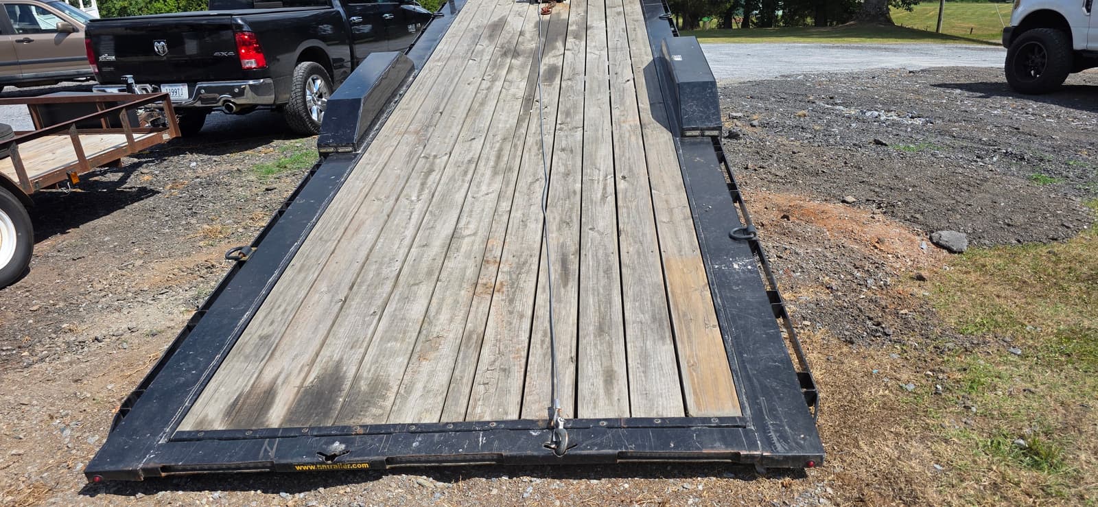 Top-down view of the 24ft H&H tilt trailer fully lowered to ground level showing the full wood deck length with tie-down rings along the sides