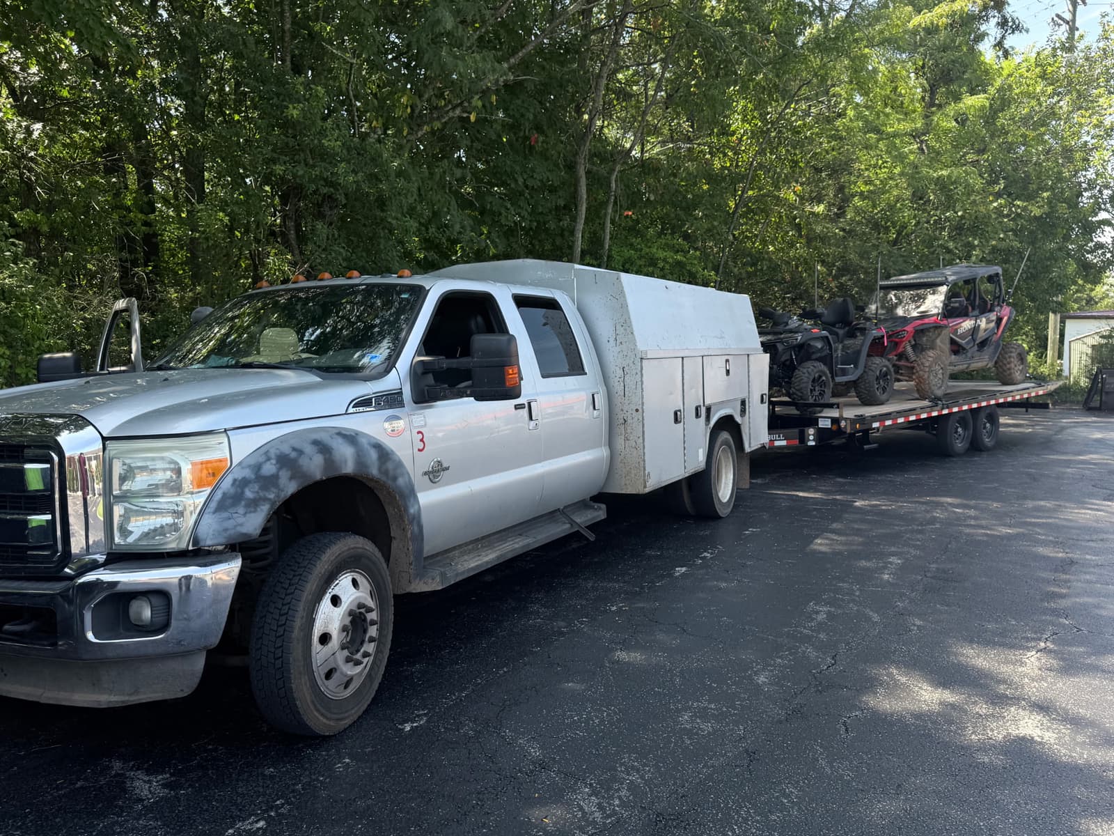 White service truck towing the 22ft Iron Bull deck over tilt trailer loaded with ATVs and side-by-side UTVs
