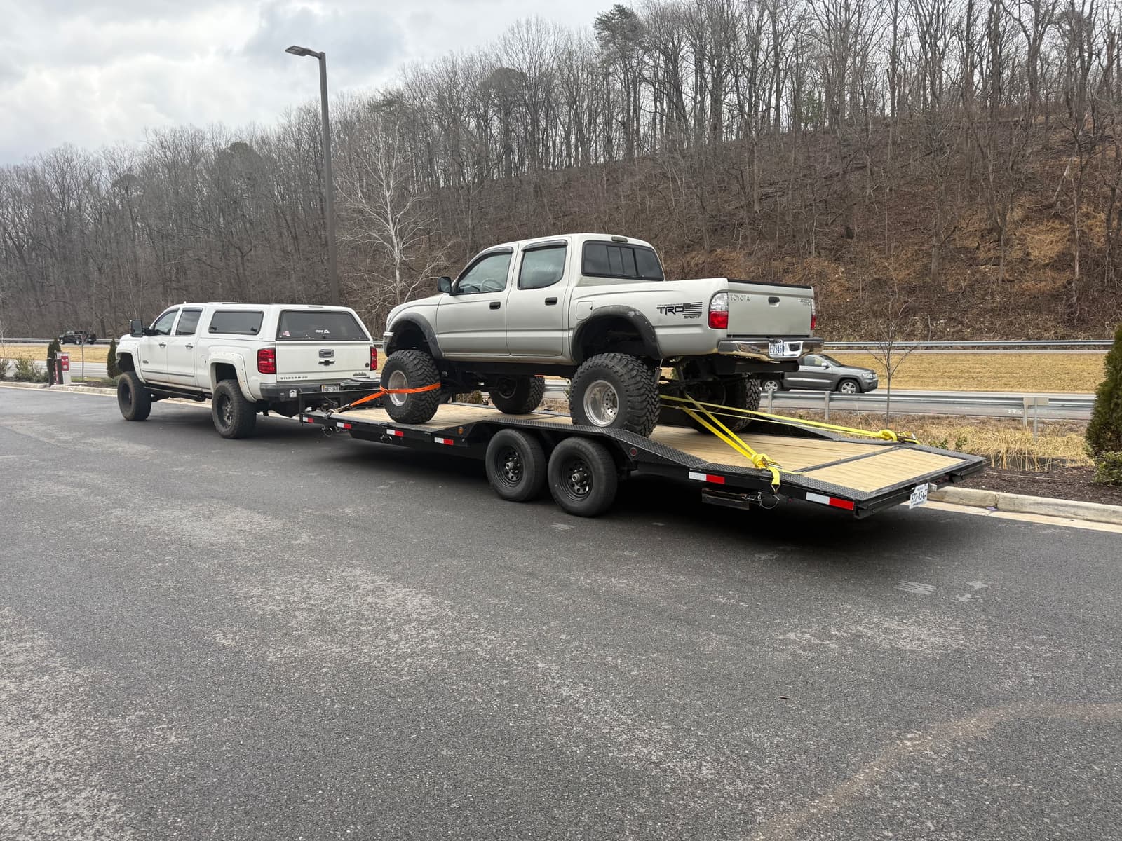 Car trailer with one vehicle towing and another vehicle positioned on the trailer deck demonstrating dual-vehicle hauling